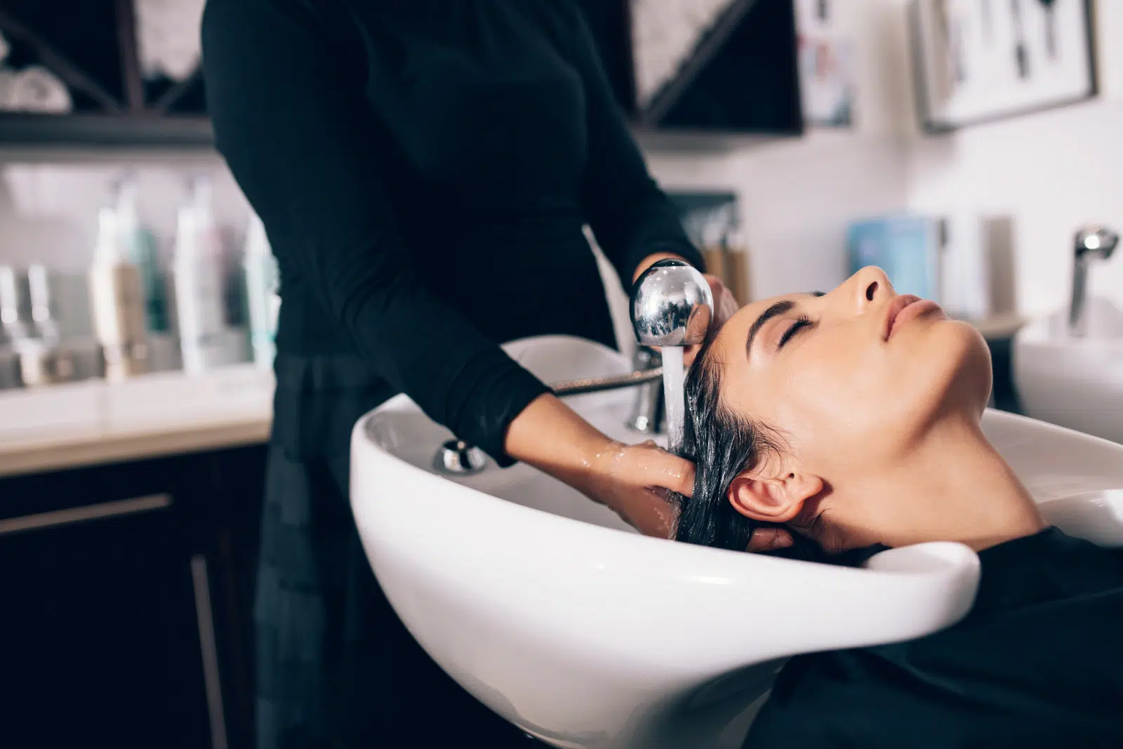 Closeup of hairdresser giving hair wash service to a customer at the salon. Woman getting hair spa treatment done at hair salon