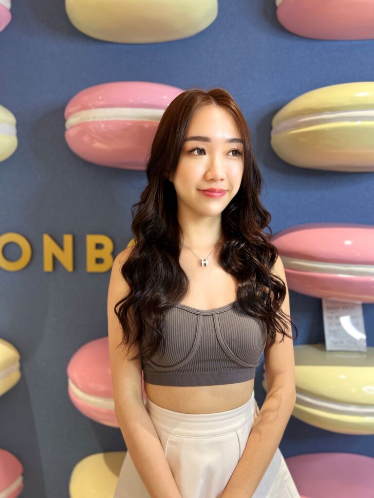 A woman with long wavy hair stands in front of a colorful macaron-themed wall at BonBon.